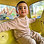 child, toddler, boy, sitting, yellow, playground, indoor, clothing, long_sleeve, pants, curious, face, smile, eyes, hair, window, background_blur, casual, happy, cute