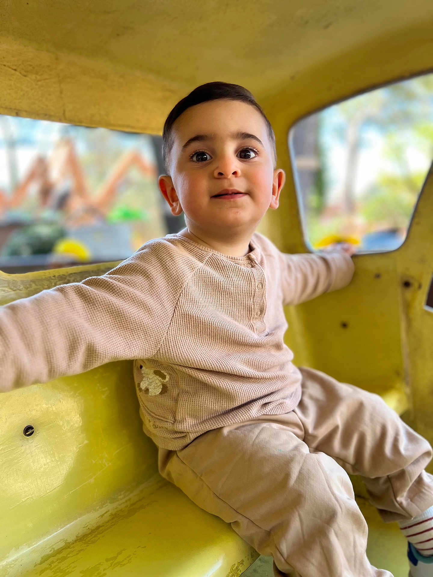 Mickael a rejoint le concours — aidez-le/la à gagner de superbes lots ! child, toddler, boy, sitting, yellow, playground, indoor, clothing, long_sleeve, pants, curious, face, smile, eyes, hair, window, background_blur, casual, happy, cute