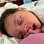 baby, sleeping, close_up, face, hand, curly_hair, blanket, pattern, floral, infant, peaceful, resting, cute, newborn, pink, skin, mouth, finger, soft_lighting, indoors