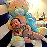 baby, infant, child, smiling, sitting, portrait, teddy_bear, plush_toy, rainbow_colors, chair, indoors, home, cozy, warm_lighting, striped_fabric, onesie, socks, happy, playful, ai_generated_content