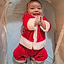 baby, infant, child, smiling, santa_outfit, red_clothing, fur_trim, bassinet, crib, mattress, happy, indoors, portrait, hands_clasped, socks, blanket, cozy, holiday, cute, joyful