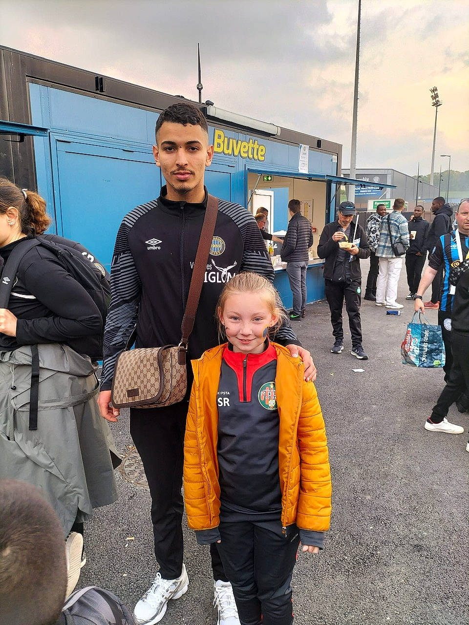 Shirley a rejoint le concours — aidez-le/la à gagner de superbes lots ! asphalt, bag, boot, cloud, electric_blue, event, headwear, jacket, luggage_and_bags, luxury_vehicle, person, personal_protective_equipment, recreation, sky, smile, team, tire, toddler, uniform, walking