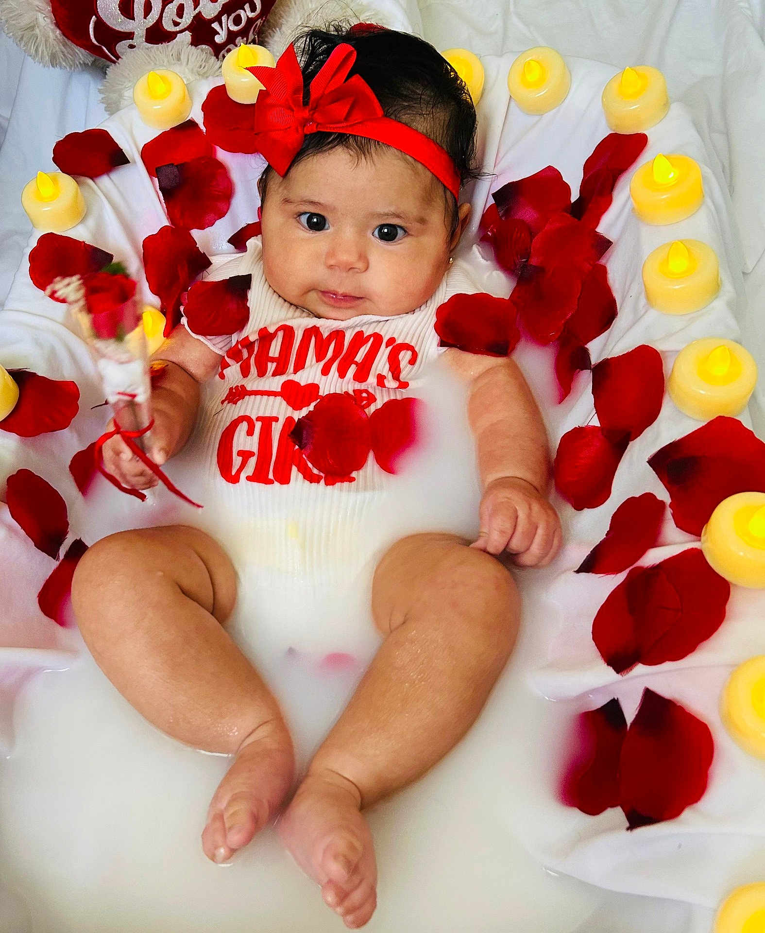 Mia joined the competition — help win amazing prizes! baby, infant, milk_bath, red_bow, rose_petals, candles, flower, cute, child, portrait, white_clothing, water, skin, headband, sitting, hand, foot, face, expression, indoor