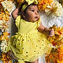 Mia is registered to the contest to win money with this photo: baby, yellow_dress, headband, autumn_leaves, flowers, infant, cute, lying_down, curious, indoors, soft_lighting, tulle_skirt, polka_dots, closeup, portrait, child, seasonal, warm_colors, adorable, happy