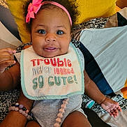 Taliyah joined the competition — help win amazing prizes! baby, child, infant, smiling, bib, headband, pink_bow, yellow_pillow, colorful_bedding, arm, bracelet, cute, happy, indoors, person, clothing, sitting, portrait, expression, skin