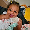 Taliyah is registered to the contest to win money with this photo: baby, child, smiling, curly_hair, hair_ties, indoor, couch, blanket, hand, face, happy, infant, clothing, person, cute, portrait, sitting, toy, home, colorful