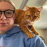 Cheeto joined the competition — help win amazing prizes! cat, orange_tabby, pet, animal, person, portrait, selfie, glasses, blue_hoodie, shoulder, indoors, mirror, whiskers, green_eyes, striped_fur, sitting, cute, funny, home, photography