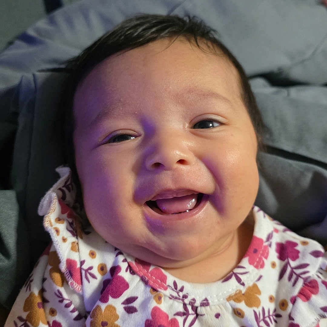 Kayelani is registered to the contest to win money with this photo: baby, blanket, child, clothing, cute, eyes, face, floral_pattern, happy, head, indoors, infant, mouth, person, portrait, sitting, skin, smiling, warm, young