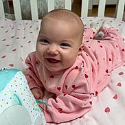 Rose a rejoint le concours — aidez-le/la à gagner de superbes lots ! baby, smiling, pink_clothing, heart_pattern, crib, blanket, strawberry_pattern, toy, cat_toy, indoor, child, cute, happy, infant, bedroom, lying_down, person, face, head, sock