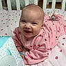 baby, smiling, pink_clothing, heart_pattern, crib, blanket, strawberry_pattern, toy, cat_toy, indoor, child, cute, happy, infant, bedroom, lying_down, person, face, head, sock