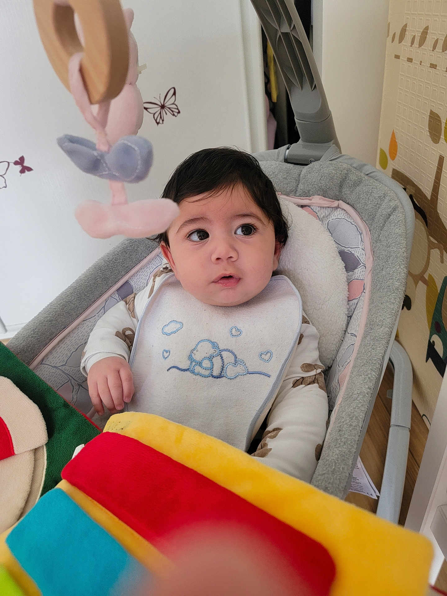 Eylen a rejoint le concours — aidez-le/la à gagner de superbes lots ! baby, infant, bib, rocker, toy, blanket, cushion, indoor, child, curious, face, person, clothing, soft_toy, wall_decor, butterfly, home, colorful, seated, young