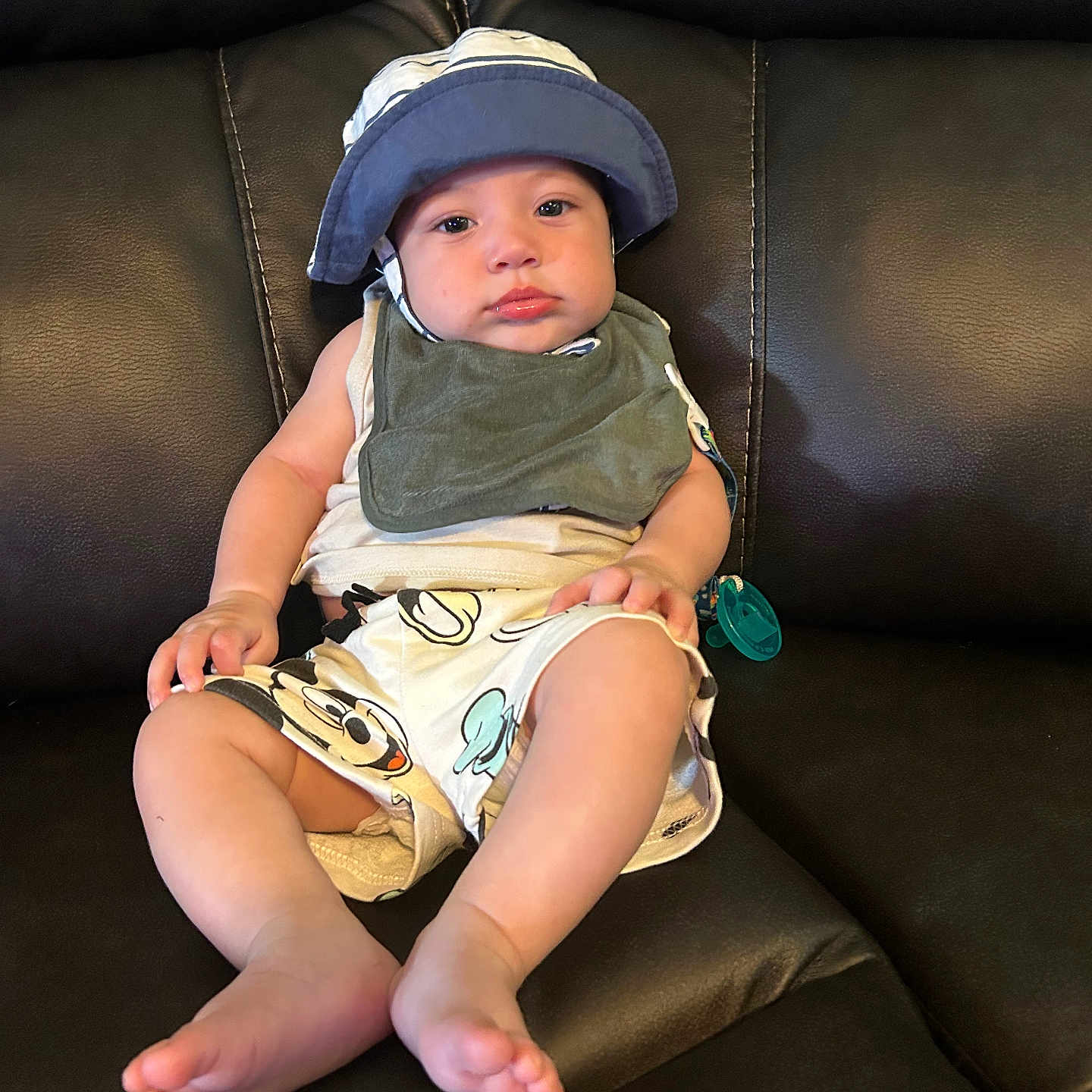 Kaleb joined the competition — help win amazing prizes! baby, child, infant, hat, bib, shorts, cartoon, sitting, leather_couch, indoor, comfortable, pout, skin, foot, hand, casual_clothing, relaxed, young, portrait, cute