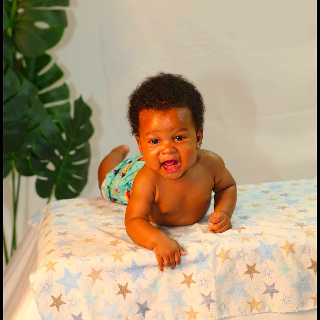 Desiah joined the competition — help win amazing prizes! baby, background, blanket, child, colorful, curly_hair, cute, happy, indoor, infant, leaf, lying_down, person, plant, reaching, skin, smiling, star_pattern, toddler, warm_lighting