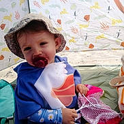 Lyana participe au concours pour gagner de l'argent avec cette photo : toddler, child, pacifier, hat, poncho, tent, beach, sand, toy, mesh_bag, animal_pattern, blue_clothing, pink, yellow, outdoor, sun_hat, cute, sitting, playful, smiling