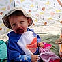 toddler, child, pacifier, hat, poncho, tent, beach, sand, toy, mesh_bag, animal_pattern, blue_clothing, pink, yellow, outdoor, sun_hat, cute, sitting, playful, smiling