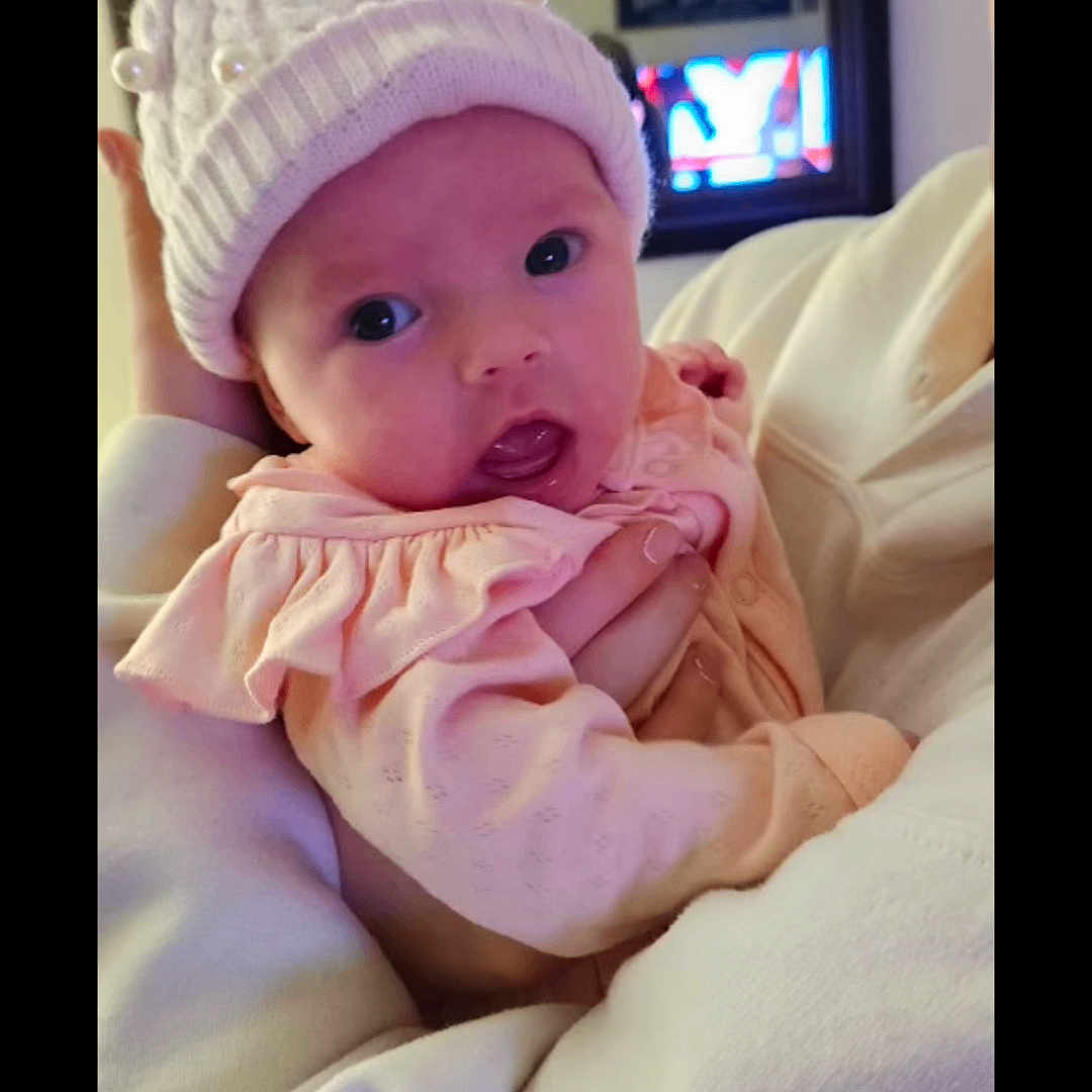 Lillyanna Marie is registered to the contest to win money with this photo: adult, baby, bow, child, cute, expression, face, hand, hat, holding, indoor, infant, mirror, pearls, person, pink_clothing, portrait, soft_lighting, sweatshirt, television