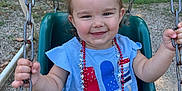 Maliyah is registered to the contest to win money with this photo: toddler, child, swing, playground, outdoor, smile, pigtails, blue_shirt, necklace, chains, green_swing, grass, trees, sunlight, happy, face, hands, summer, casual_clothing, park