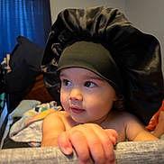 Maliyah is registered to the contest to win money with this photo: toddler, child, baby, face, hand, bonnet, black_bonnet, indoor, curious, soft_light, skin, portrait, person, furniture, blanket, bedroom, cozy, expression, young_child, candid