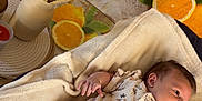 Mani a rejoint le concours — aidez-le/la à gagner de superbes lots ! baby, blanket, onesie, green_socks, face, infant, vase, dried_grasses, oranges, seashells, starfish, table, indoor, soft_texture, relaxing, resting, cute, child, patterned_clothing, warm