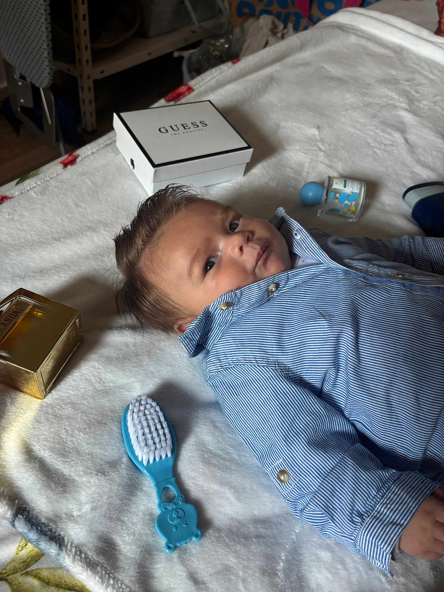 Mani a rejoint le concours — aidez-le/la à gagner de superbes lots ! baby, child, blue_shirt, striped_clothing, lying_down, white_blanket, baby_brush, perfume_bottle, guess_box, indoor, curly_hair, face, expression, soft_texture, baby_grooming, portrait, cute, infant, closeup, relaxing