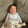 baby, smile, toy, giraffe_toy, blanket, couch, child, happy, indoor, infant, clothing, face, person, sitting, cute, young_child, soft_toy, playful, comfort, bright_eyes