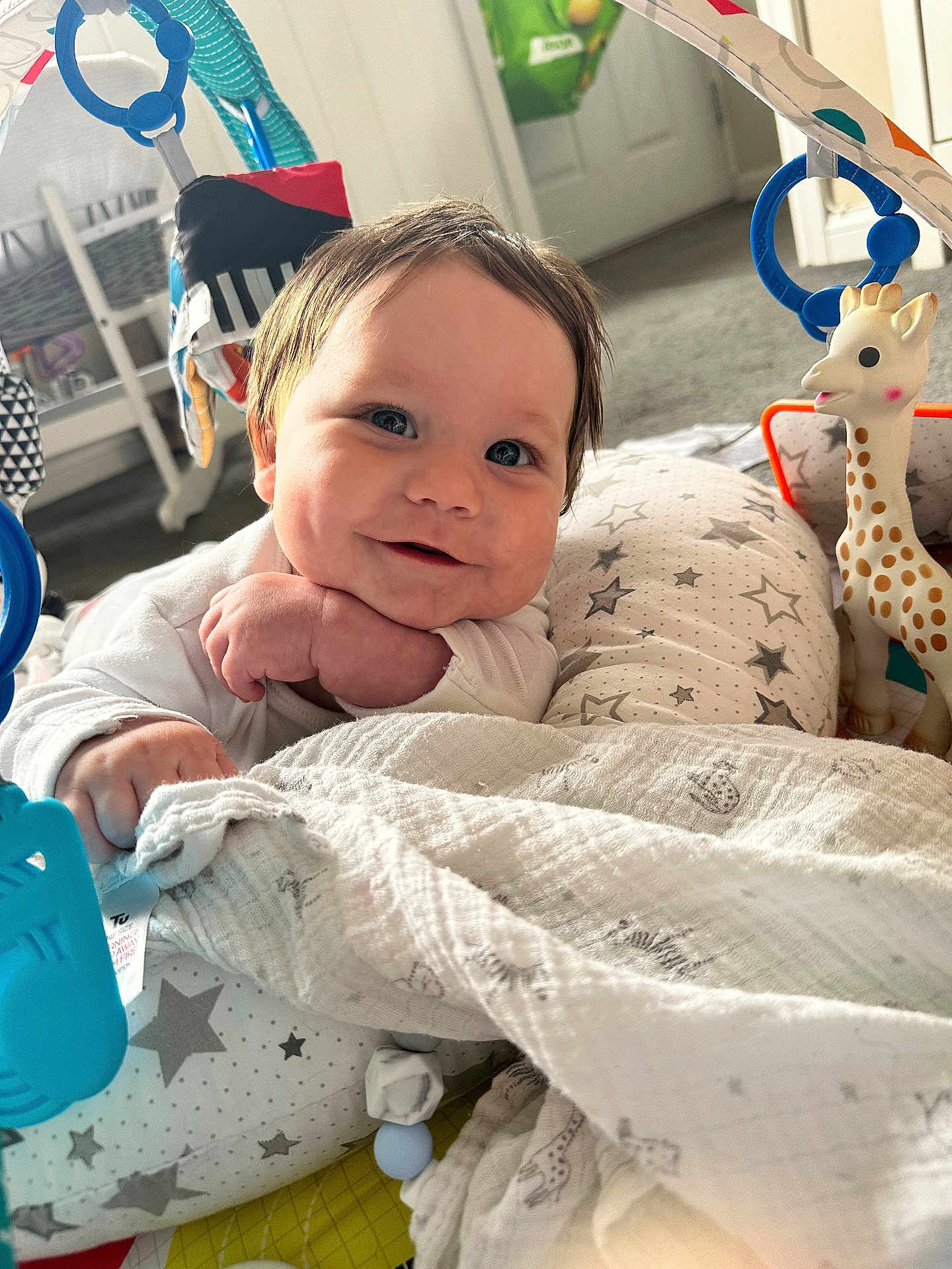 Tayler joined the competition — help win amazing prizes! baby, smiling, face, cushion, blanket, toy, giraffe, indoor, carpet, child, happy, playing, closeup, infant, hand, head, white_clothing, floor, baby_gym, colorful