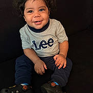 Josiah joined the competition — help win amazing prizes! toddler, child, smiling, curly_hair, sitting, gray_shirt, lee_logo, navy_pants, black_shoes, basketball_shoes, indoor, couch, happy, person, portrait, young_child, casual_clothing, cute, hands, feet
