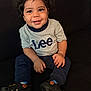 toddler, child, smiling, curly_hair, sitting, gray_shirt, lee_logo, navy_pants, black_shoes, basketball_shoes, indoor, couch, happy, person, portrait, young_child, casual_clothing, cute, hands, feet