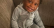 Bryson joined the competition — help win amazing prizes! child, toddler, smiling, portrait, sitting, couch, indoors, tracksuit, gray_clothing, hoodie, curly_hair, happy, face, teeth, socks, furniture, living_room, cozy, candid, photography