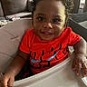 Bryson joined the competition — help win amazing prizes! baby, child, infant, smiling, happy, portrait, high_chair, red_shirt, curly_hair, brown_skin, face, hands, indoor, home, living_room, couch, sunlight, tray, seated, photography