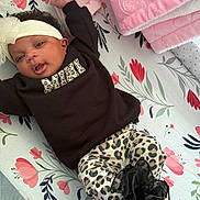 Blessyn is registered to the contest to win money with this photo: baby, infant, child, portrait, lying_down, floral_blanket, bow_headband, black_shirt, leopard_print, fashion, smiling, open_mouth, face, eyes, indoor, nursery, changing_mat, pink_blanket, clothing, photography