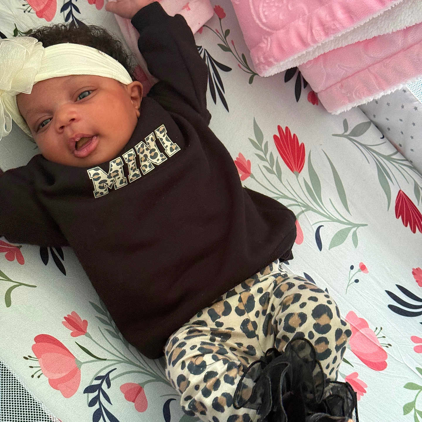 Blessyn is registered to the contest to win money with this photo: baby, infant, child, portrait, lying_down, floral_blanket, bow_headband, black_shirt, leopard_print, fashion, smiling, open_mouth, face, eyes, indoor, nursery, changing_mat, pink_blanket, clothing, photography