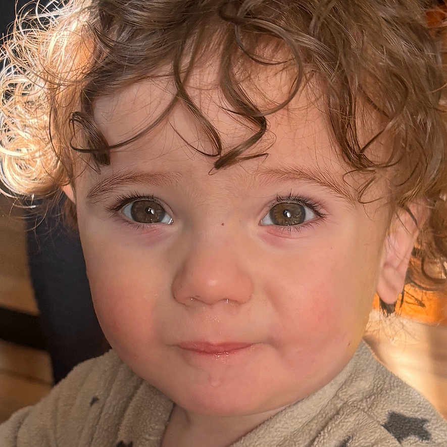 Jules a rejoint le concours — aidez-le/la à gagner de superbes lots ! background_blur, brown_eyes, child, close_up, clothing, cozy, curiosity, curly_hair, cute, drool, expression, face, indoor, onesie, person, portrait, soft_lighting, star_pattern, toddler, young_child