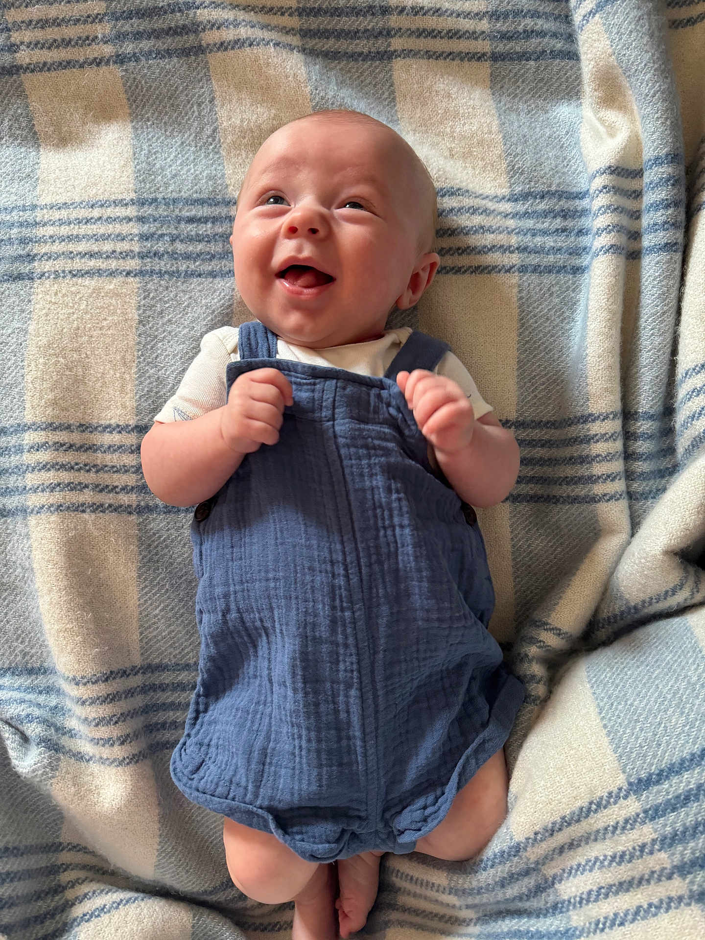 Rowan is registered to the contest to win money with this photo: baby, infant, smiling, blue_romper, blanket, checkered_pattern, happy, cute, lying_down, soft_texture, small_hands, bare_legs, indoors, child, young, head, face, cheerful, cozy, portrait