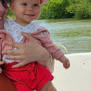 Elina a rejoint le concours — aidez-le/la à gagner de superbes lots ! baby, child, smiling, cap, pink, white, red_shorts, outdoor, river, trees, greenery, adult, holding, boat, water, nature, sunlight, happy, person, summer
