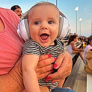 Waylon joined the competition — help win amazing prizes! baby, headphones, striped_clothing, smiling, happy, person, adult_hand, nail_polish, outdoor, bench, spectators, evening, light_poles, crowd, casual_wear, closeup, infant, joy, parent, fun