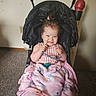 toddler, child, stroller, blanket, glasses, indoor, carpet, wall, filing_cabinet, pink_blanket, smiling, happy, baby, clothing, toy, cozy, sitting, person, cute, playful