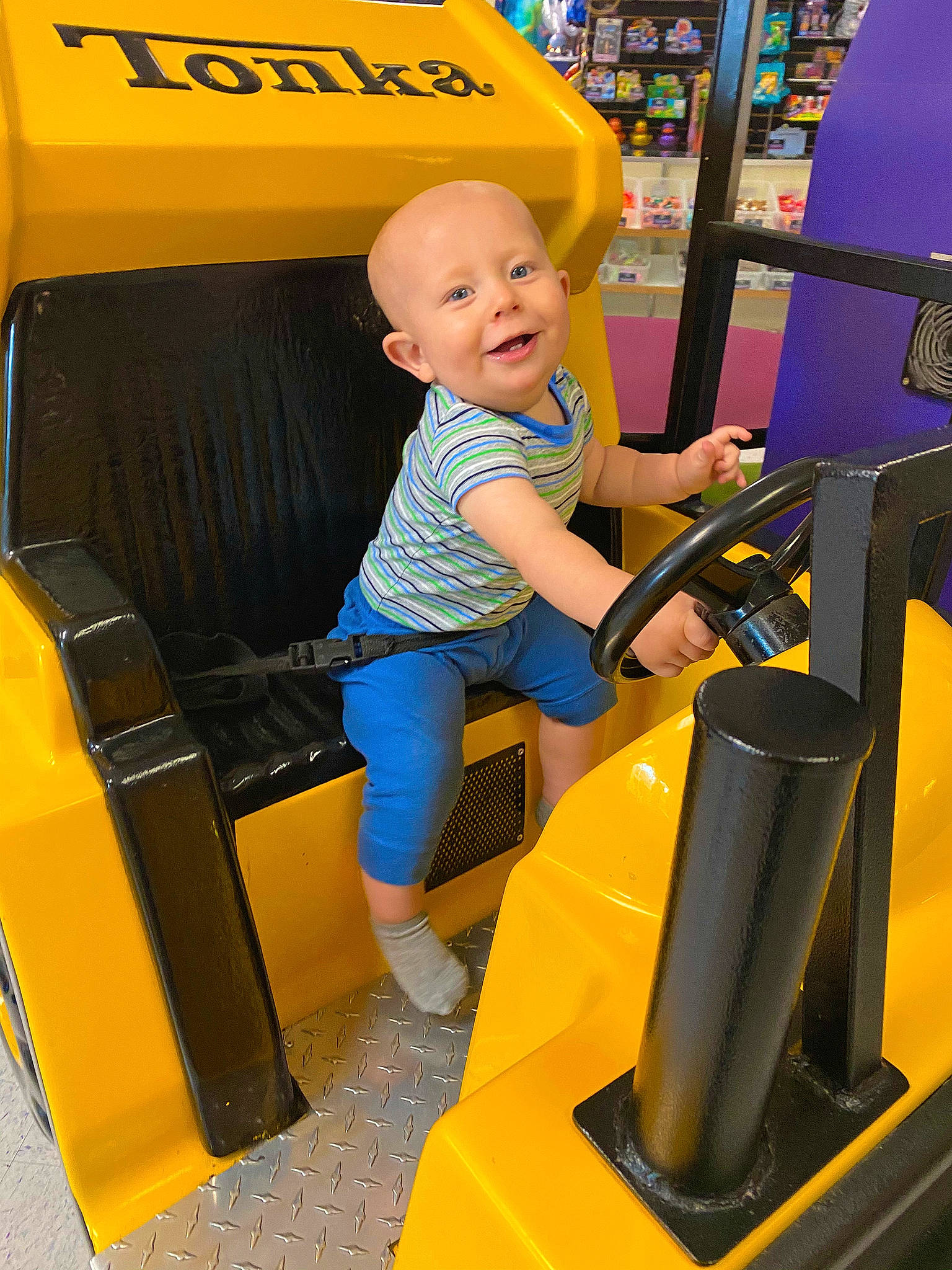Paul is registered to the contest to win money with this photo: automotive_design, baby, child, chute, electric_blue, fun, leisure, motor_vehicle, person, play, recreation, riding_toy, shelf, shorts, sitting, smile, snapshot, standing, toddler, travel