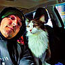 man, cat, car_interior, selfie, beanie, hoodie, fluffy_cat, coffee_cup, seat, window, console, pet, indoor, casual, portrait, companion, cozy, relaxed, animal, human