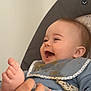 baby, infant, laughing, smiling, bib, foot, toes, hand, face, cheeks, head, onesie, cushion, seat, portrait, closeup, happy, home_interior, candid, babycare