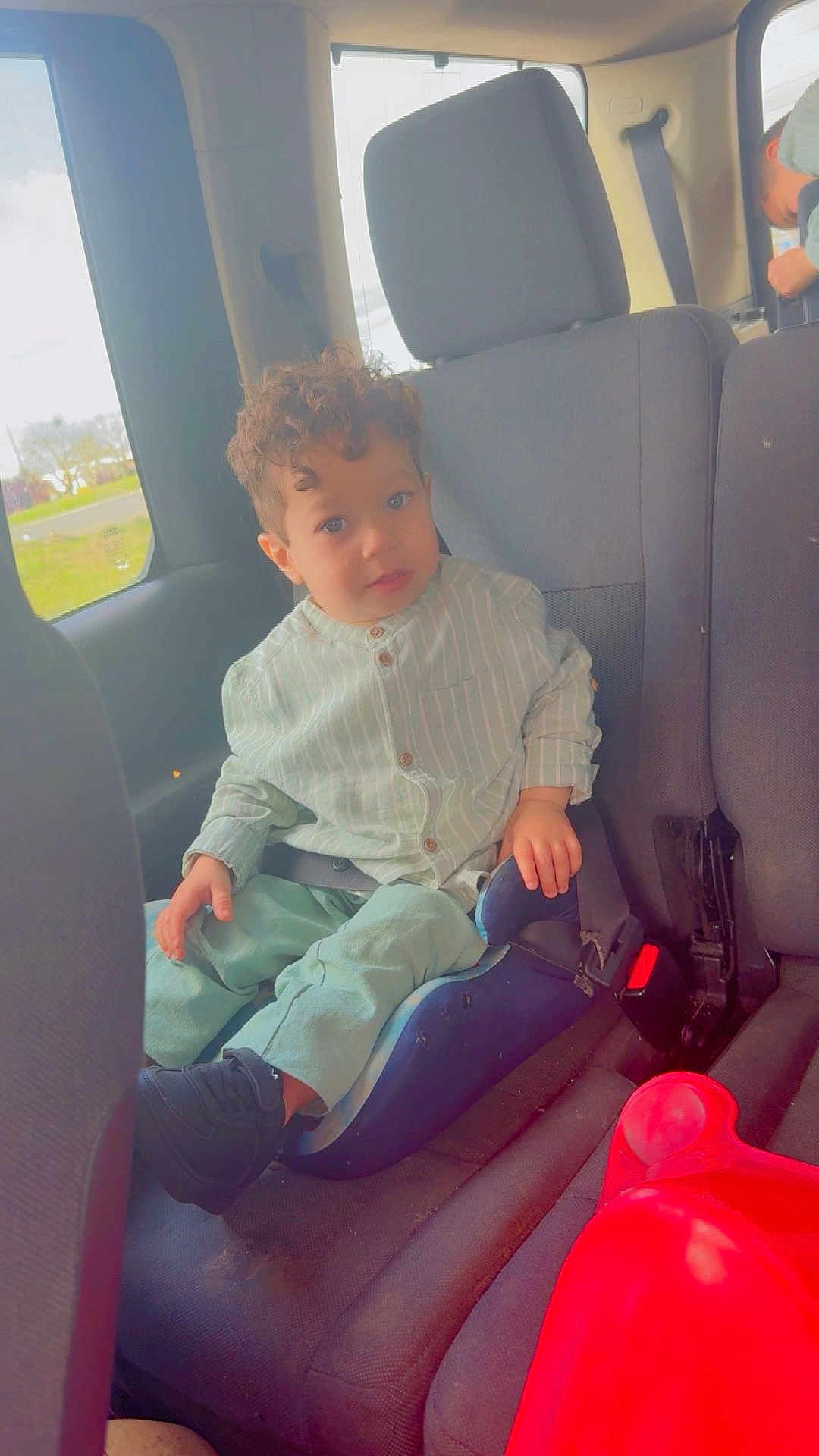 Isaac a rejoint le concours — aidez-le/la à gagner de superbes lots ! child, car_seat, vehicle_interior, curly_hair, casual_clothing, seatbelt, window, red_object, young_child, looking_at_camera, car_seat_booster, indoor, sitting, seat, curious_expression, daylight, casual, young_person, car, transportation