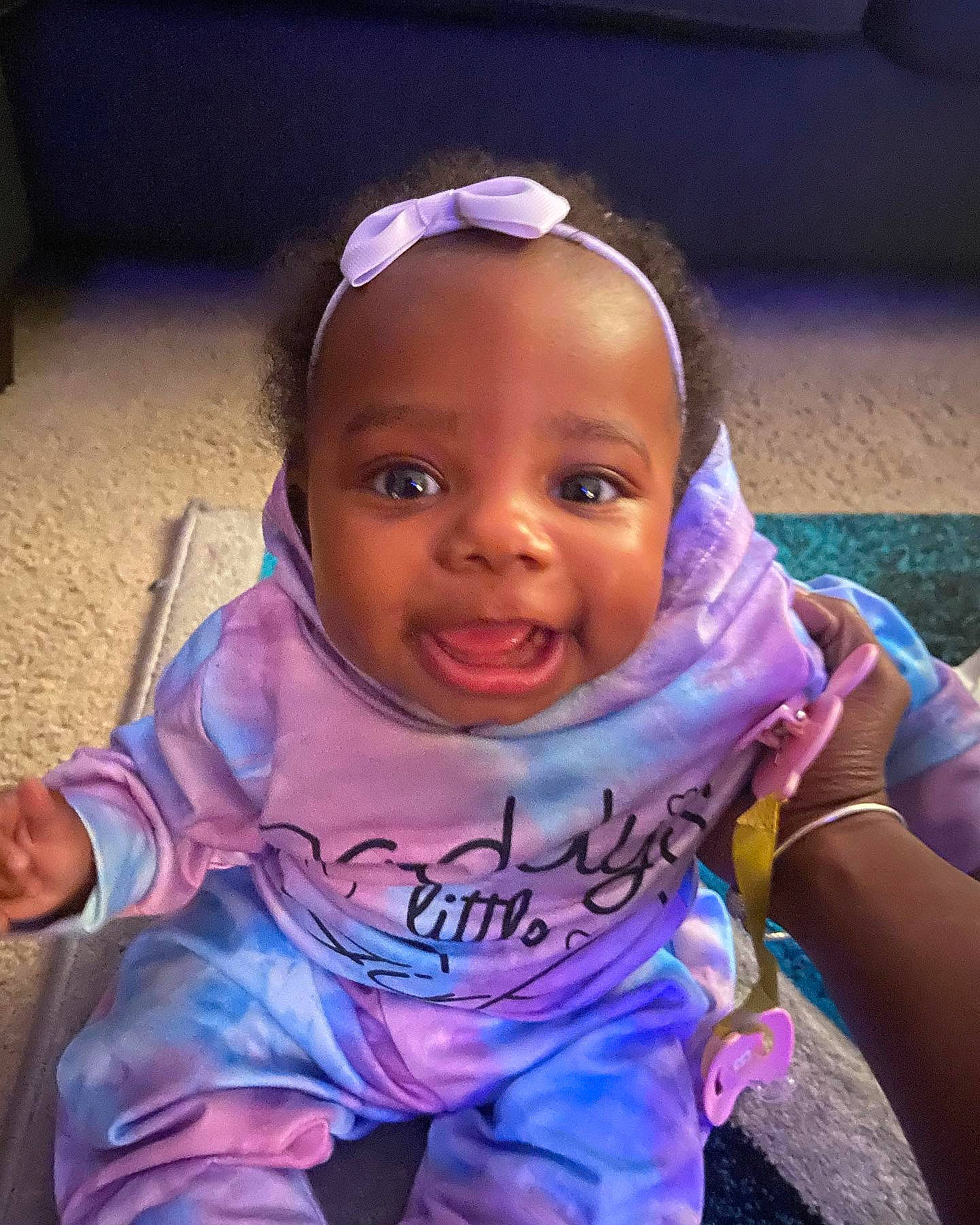 Laila is registered to the contest to win money with this photo: baby, baby_toddler_clothing, child, chin, electric_blue, eyebrow, eyelash, fashion_accessory, fun, happy, leisure, magenta, mouth, person, pink, purple, sitting, skin, smile, t_shirt