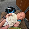 baby, infant, sleeping, pacifier, diaper, onesie, portrait, indoor, waiting_room, carpet, chair, baby_carrier, adult, lap, resting, peaceful, cozy, candid, wood_paneling, photography