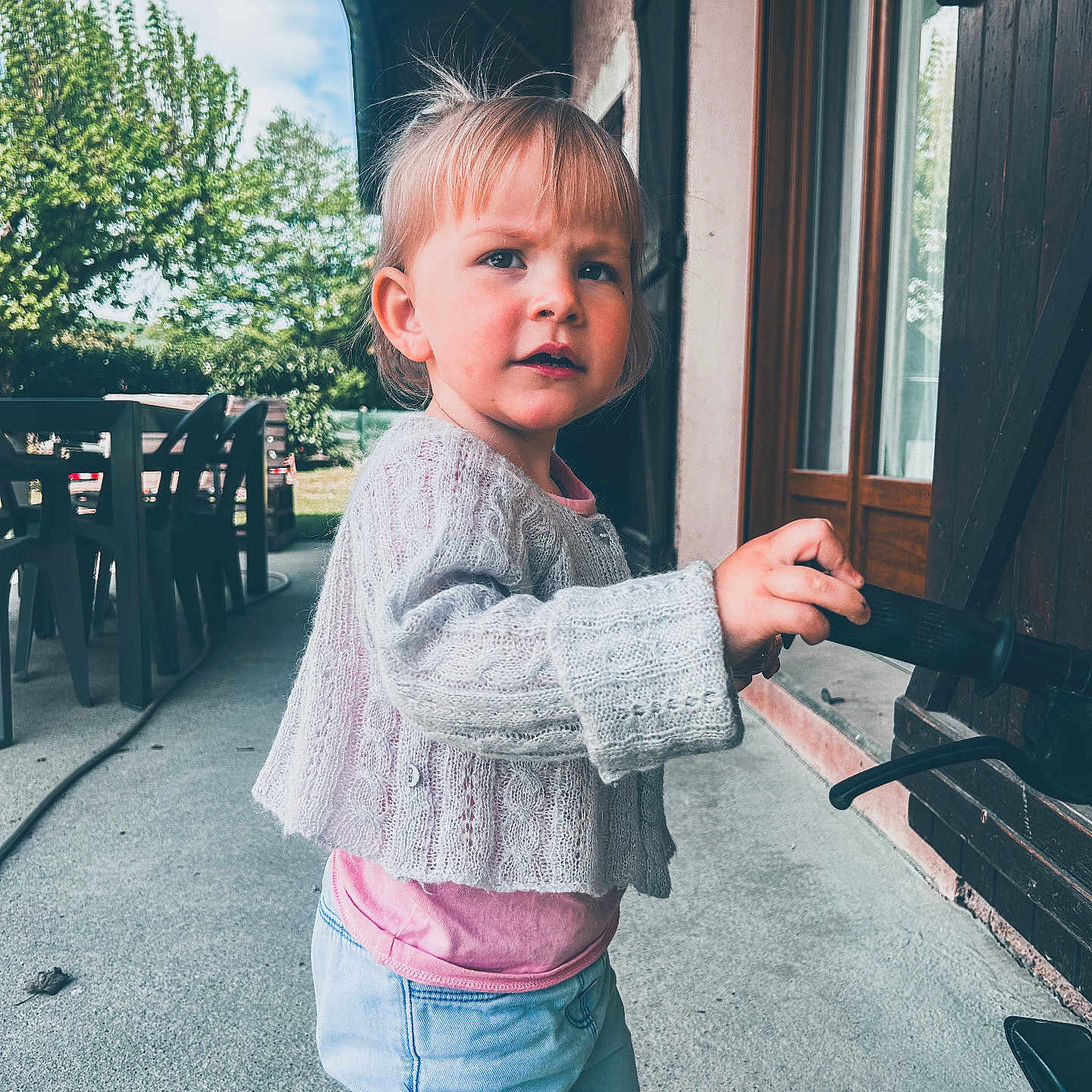 Elise a rejoint le concours — aidez-le/la à gagner de superbes lots ! toddler, child, outdoor, sweater, jeans, handle, door, window, tree, sky, fence, table, chair, curious, person, building, concrete, daylight, young_child, casual_clothing