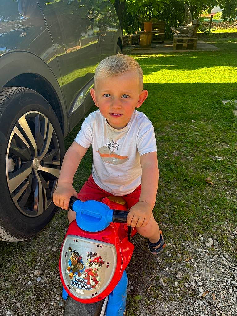 étann a rejoint le concours — aidez-le/la à gagner de superbes lots ! alloy_wheel, automotive_exterior, automotive_lighting, automotive_tire, car, fender, grass, hubcap, motor_vehicle, person, plant, rim, smile, t_shirt, tire, tire_care, toddler, tree, vehicle, vehicle_door