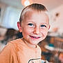 child, boy, smile, indoor, portrait, blonde_hair, blue_eyes, casual_clothing, skateboard_graphic, happy, young, person, face, tshirt, room, background_blur, cute, cheerful, kid, closeup