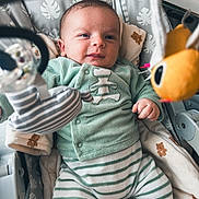 Elyo a rejoint le concours — aidez-le/la à gagner de superbes lots ! baby, infant, baby_seat, toy, plush_toy, striped_clothing, green_clothing, blanket, comfort, indoor, child, cute, smiling, face, hand, soft_toys, fabric, pattern, relaxing, portrait