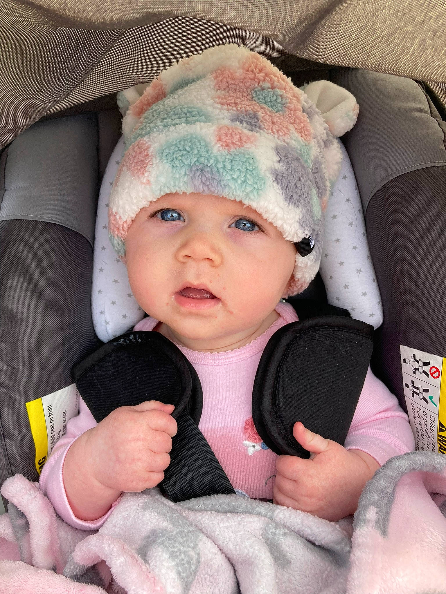 Parker is registered to the contest to win money with this photo: baby_in_car_seat, baby_toddler_clothing, cap, cheek, chin, comfort, eye, face, finger, gesture, hand, head, headgear, headwear, human_body, lip, nose, person, pink, skin