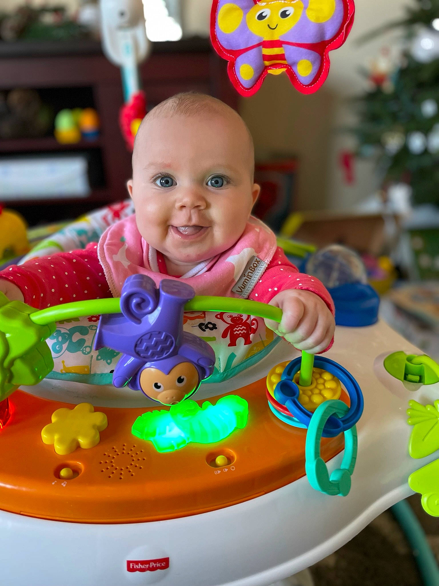 Parker is registered to the contest to win money with this photo: baby, baby_playing_with_toys, baby_products, baby_toddler_clothing, baby_toys, child, christmas_tree, event, fun, happy, holiday, joy, leisure, person, play, recreation, room, shelf, sitting, smile