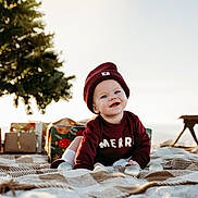Jaxon joined the competition — help win amazing prizes! baby, smiling, maroon_clothing, beanie, blanket, outdoor, holiday, christmas_tree, gifts, festive, crawling, child, happy, toy, decorations, nature, sunlight, portrait, cute, seasonal
